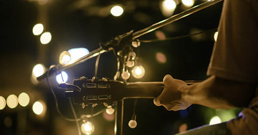 Rear view of the man sitting play acoustic guitar on the outdoor concert with a microphone stand in the front,