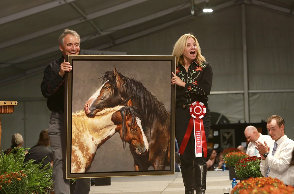 Two volunteers in Western uniforms carry "Embrace," the 2022 People's Choice Award-Winning oil painting of two wild horses by artist Mark McKenna