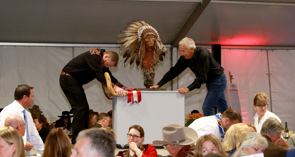 Two volunteers in Western uniforms carry "Wisdom in the Wind," the 2022 3D Award-Winning bronze of a native chief by sculptor Campbell Dosch